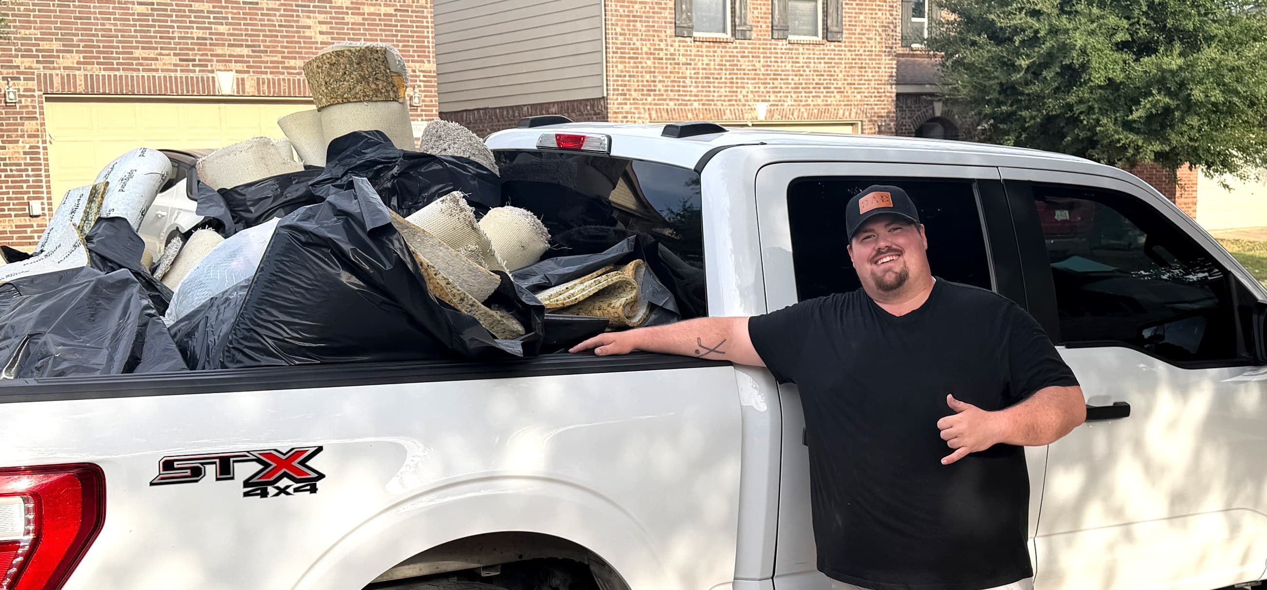 Blaze Junk & Haul crew member giving a shaka next to a pickup truck loaded with carpet and junk hauled away from a Fort Worth, TX home