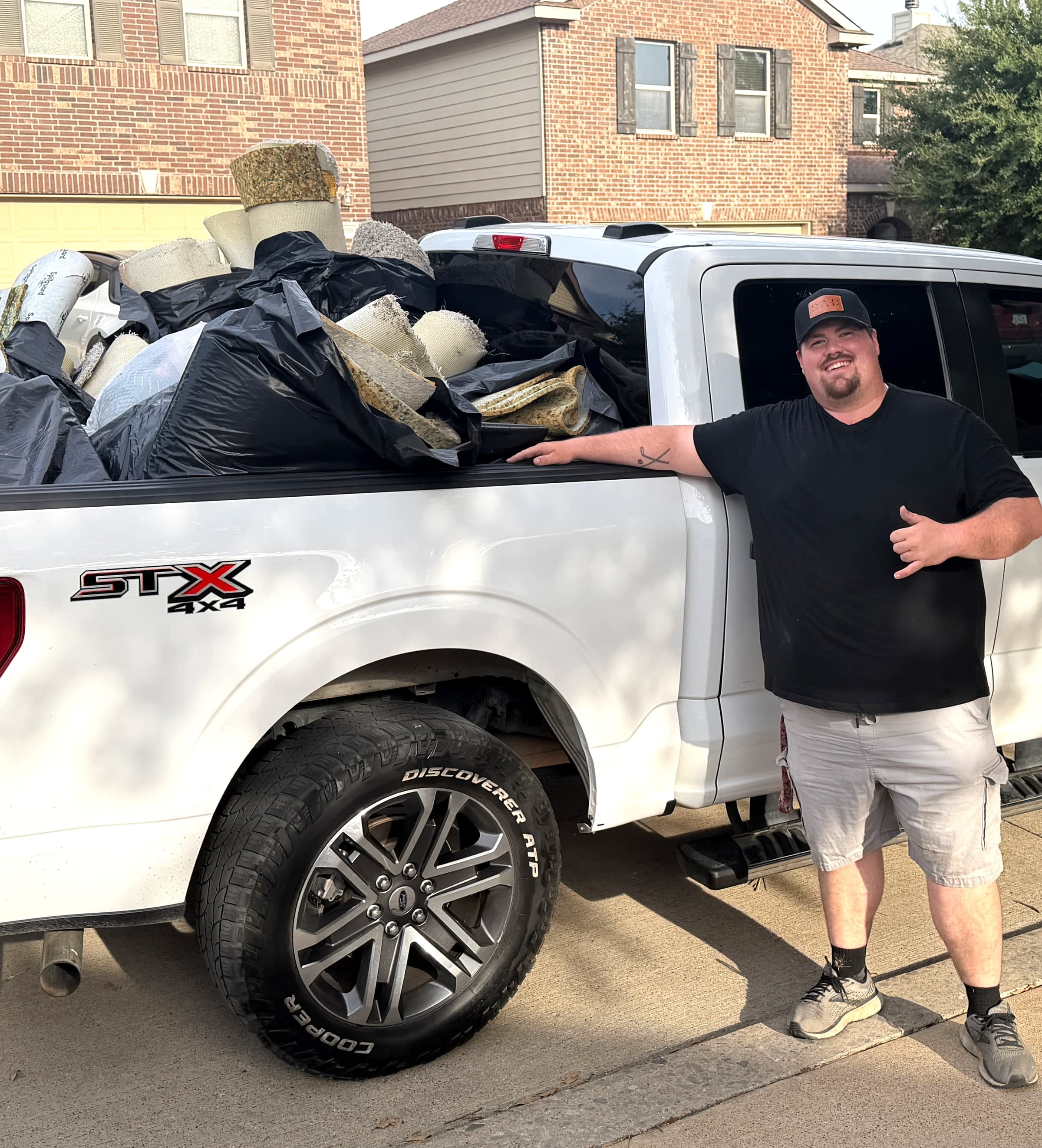 Blaze Junk & Haul crew member giving a shaka next to a pickup truck loaded with carpet and junk hauled away from a Fort Worth, TX home